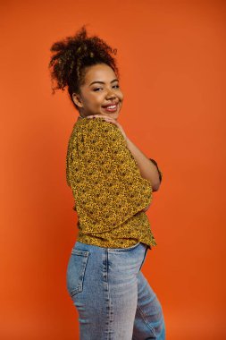 Stylish African American woman posing against vibrant orange backdrop. clipart