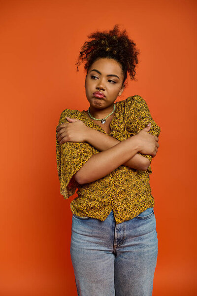 Stylish African American woman poses confidently with arms crossed against vibrant orange backdrop.