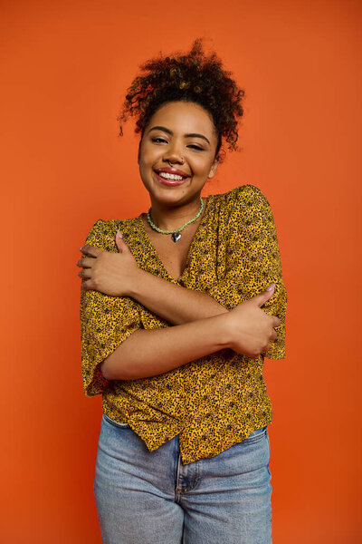 Stylish African American woman with crossed arms against vibrant orange backdrop.