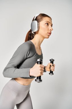Sportif bir kadın, elinde kulaklıkla dambıllar tutarak egzersiz yapmaya hazırlanıyor..