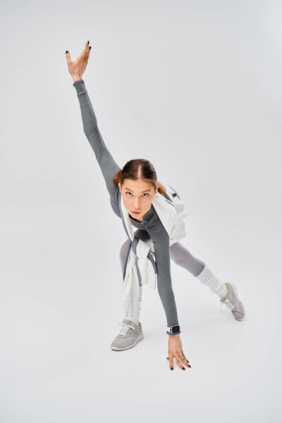 A sporty young woman in active wear dancing gracefully in a studio on a grey background.