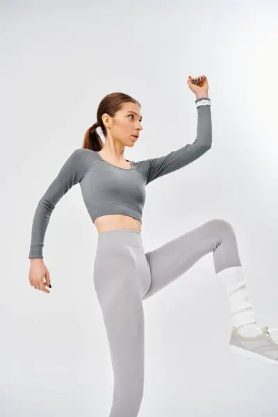 stock image A sporty young woman in a gray top and grey leggings poses gracefully on a soothing gray background.