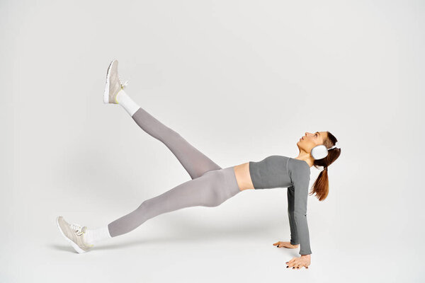 A sporty young woman in activewear demonstrating a side plank exercise on a grey background.