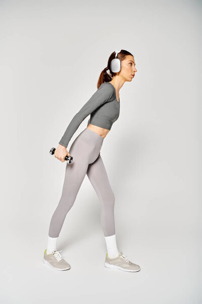 A sporty young woman in active wear with headphones working out energetically on a grey background.
