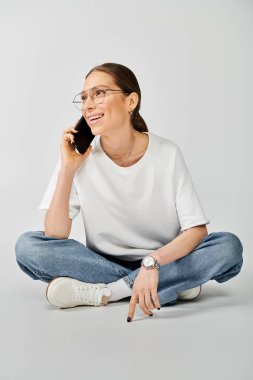 Beyaz tişörtlü bir kadın yerde oturmuş, telefonla konuşuyor..