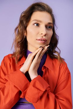A stylish young woman in a vibrant orange jacket striking a pose on a purple background. clipart