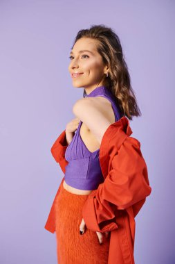 Canlı turuncu bir etek ve mor bir arka planla öne çıkan şık bir genç kadın..