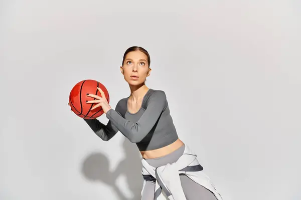 一名身穿运动衫的年轻女子 右手拿着篮球 背对着灰色背景 — 图库照片