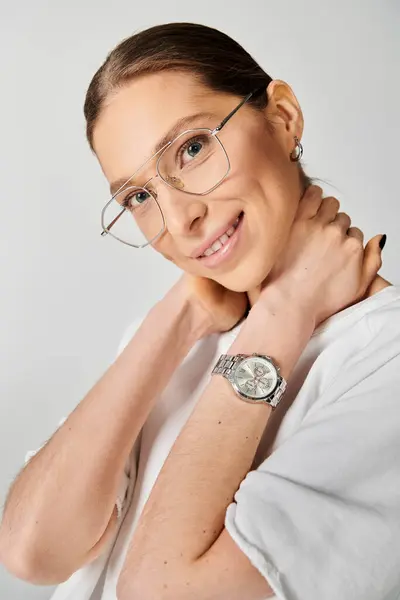 stock image A young woman exudes confidence in a white shirt and glasses against a grey background.