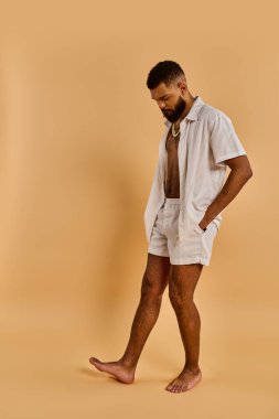 Beyaz gömlek ve şort giymiş bir adam, doğal güneş ışığı altında zarif bir şekilde duruyor, sakinlik ve rahatlama hissi yayıyor..