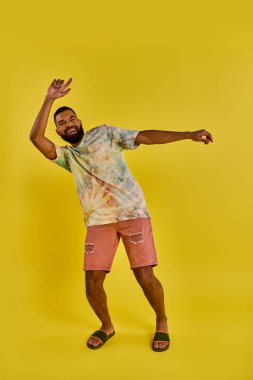 Pembe şortla eşleştirilmiş canlı bir kravat gömleği giyen bir adam rahat ve renkli bir aura yayıyor..