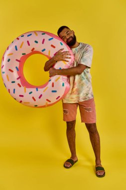 A man joyfully holds a giant donut in front of a vibrant yellow background, showcasing his love for the sweet treat. clipart