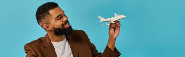 A man is holding a detailed model of a white airplane, showcasing intricate design and craftsmanship. He gazes off, lost in thoughts of aviation and adventure. clipart