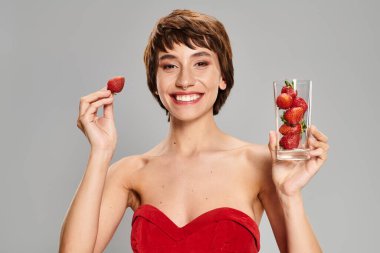 Kırmızı elbiseli genç bir kadın elinde bir bardak çilek tutuyor..