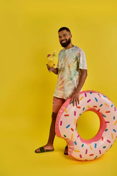 男は巨大なドーナツの隣に畏敬の念を抱いていて その巨大な大きさに飲み込まれています ドーナツはカラフルで魅力的で 食べるように懇願しています — ストック写真