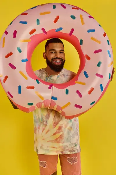stock image A man playfully hides his face behind a massive donut, showcasing his whimsical and humorous side while enjoying a tasty treat.