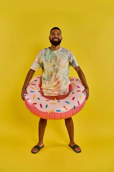 一个男人快乐地拿着一个色彩艳丽的甜甜圈 与阳光灿烂的蓝天形成鲜明对比 在水边体现着放松和欢乐 — 图库照片