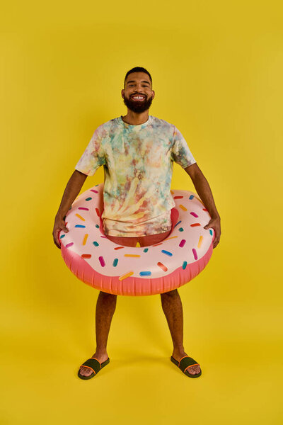 A man joyfully holds a colorful donut-shaped inflatable ring, contrasting against a sunny blue sky, embodying relaxation and fun by the water.