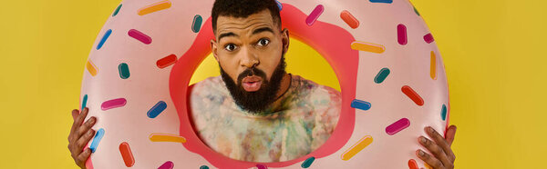 Мужчина игриво держит гигантский пончик перед лицом, закрывая глаза и рот, создавая юмористический и причудливый эффект.