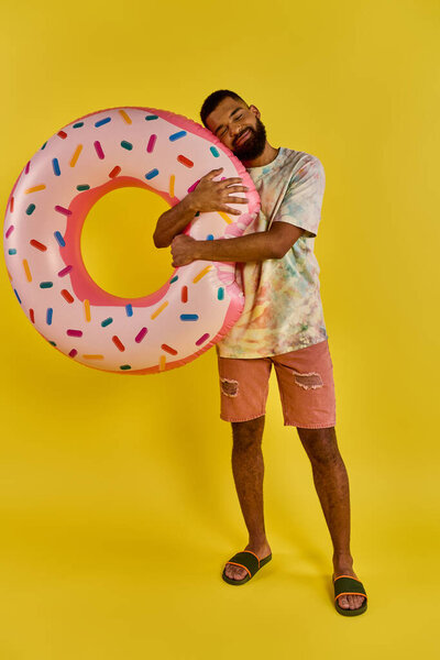 A man joyfully holds a giant donut in front of a vibrant yellow background, showcasing his love for the sweet treat.
