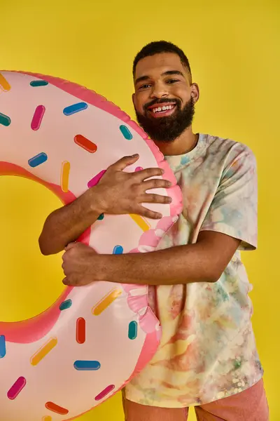stock image A man of unknown age is holding a colossal, delicious-looking donut in front of a bright yellow background.