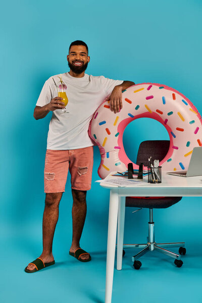A man standing next to a desk, looking excited, with a giant donut placed on it.