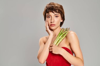 A stylish young woman holds a bunch of fresh asparagus in a vibrant setting. clipart