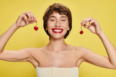 Young woman striking a pose with a cherry balanced on her head against a vibrant backdrop. clipart