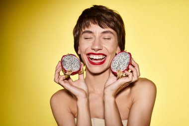 A woman playfully holds two dragon fruits in front of her face. clipart