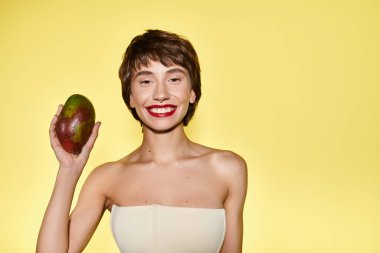 Beyaz elbiseli genç bir kadın, canlı bir arka plana karşı mango tutuyor..
