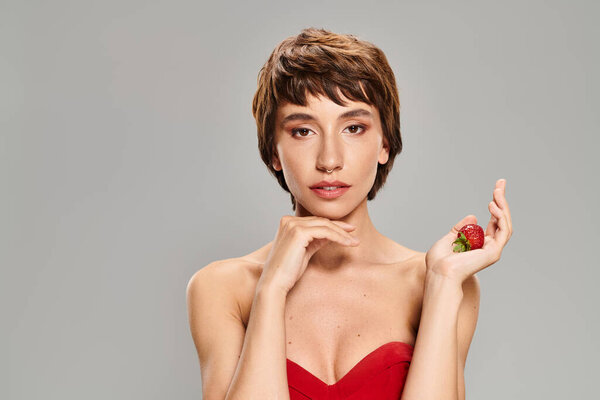 Женщина в красном платье держит фрукт на ярком фоне.