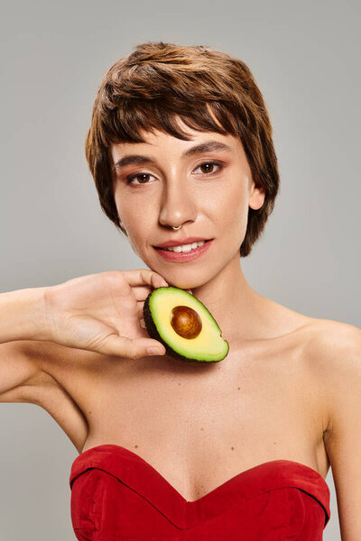 Молодая женщина в красном платье элегантно держит авокадо.