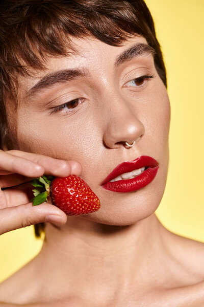 Молодая женщина обнимает сочную клубнику на щеке, излучающую блаженство.