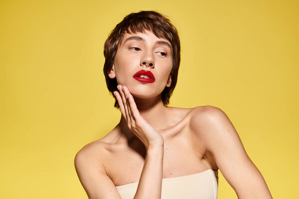 A fashionable young woman with red lipstick on her face poses elegantly on a vibrant backdrop.