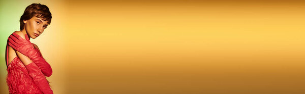 Stylish woman in red dress, hands on hips, on vibrant background.