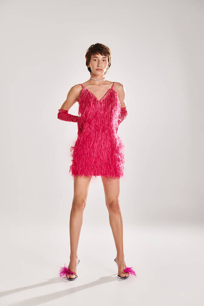 A fashionable young woman poses in an elegant pink feather dress against a vibrant backdrop.