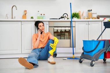 Gündelik giysiler içinde şık bir kadın yerde oturuyor, bir telefon konuşmasına dalmış..