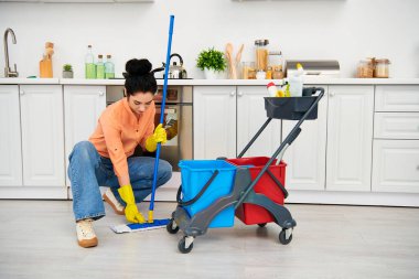 Havalı giyinmiş şık bir kadın paspas ve kovayla zarifçe yerleri temizliyor, ev işlerine zarafet katıyor..