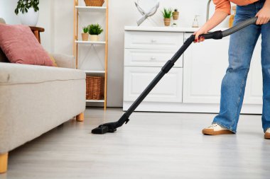 Havalı giyinmiş şık bir kadın evinin zeminini temizlemek için elektrikli süpürge kullanıyor..
