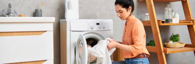 Gündelik giysiler içinde şık bir kadın kumaşı bir kurutma makinesine koyuyor..