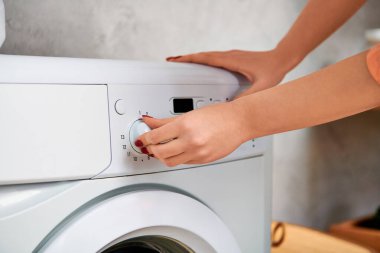 Sıradan giyinmiş şık bir kadın, bir düğmeyi dikkatlice çamaşır makinesine takar..