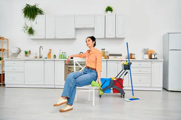 カジュアルな服装のスタイリッシュな女性は落ち着きと満足感を誇る清潔なキッチンの椅子に快適に座っています — ストック写真