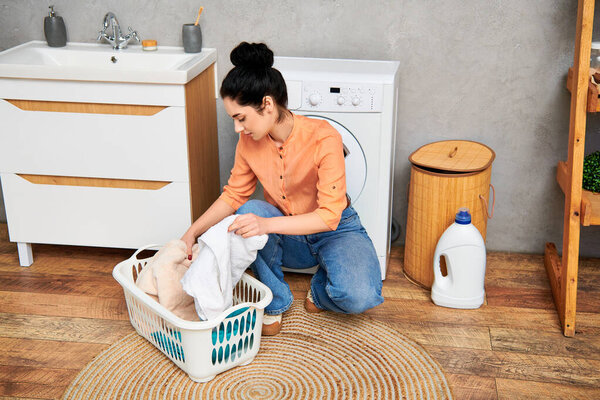 Стильная женщина в повседневной одежде сидит на полу рядом с корзиной для белья, отдыхая от уборки дома..