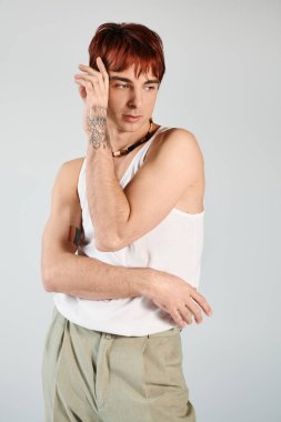 A young man strikes a pose in a studio, wearing a tank top and khaki pants against a grey background. clipart