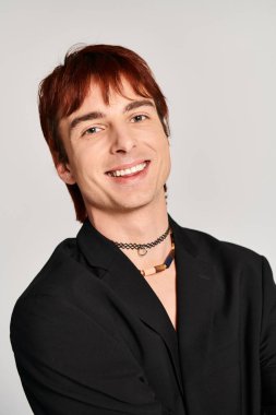 Kırmızı saçlı şık bir genç adam gri bir arka plana karşı siyah gömlekli poz veriyor..