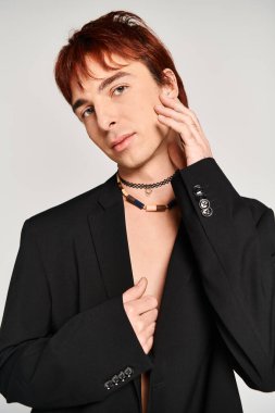 Stylish young man strikes a pose in a black suit and choker against a grey studio backdrop. clipart