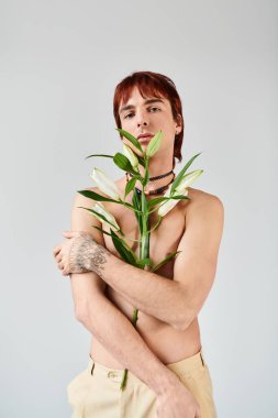 A shirtless man cradles a plant in his hands, showcasing his connection to nature in a studio setting with a grey background. clipart