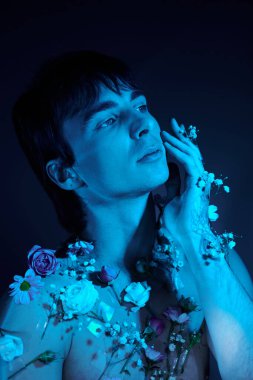Mavi ışığı olan bir stüdyoda çiçeklerle çevrili genç bir adam.