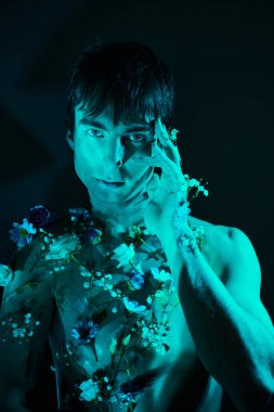 young shirtless man surrounded by blooming flowers posing in studio with blue light clipart