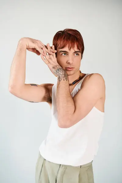 stock image A stylish young man in a tank top strikes a confident pose against a grey studio background.